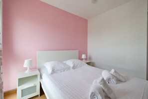 A neatly made bed with white linens and two rolled towels, a bedside table with a lamp, and a nightstand with a lamp. - Apartment '3 chambres Vue Montagnes -' (Annecy)