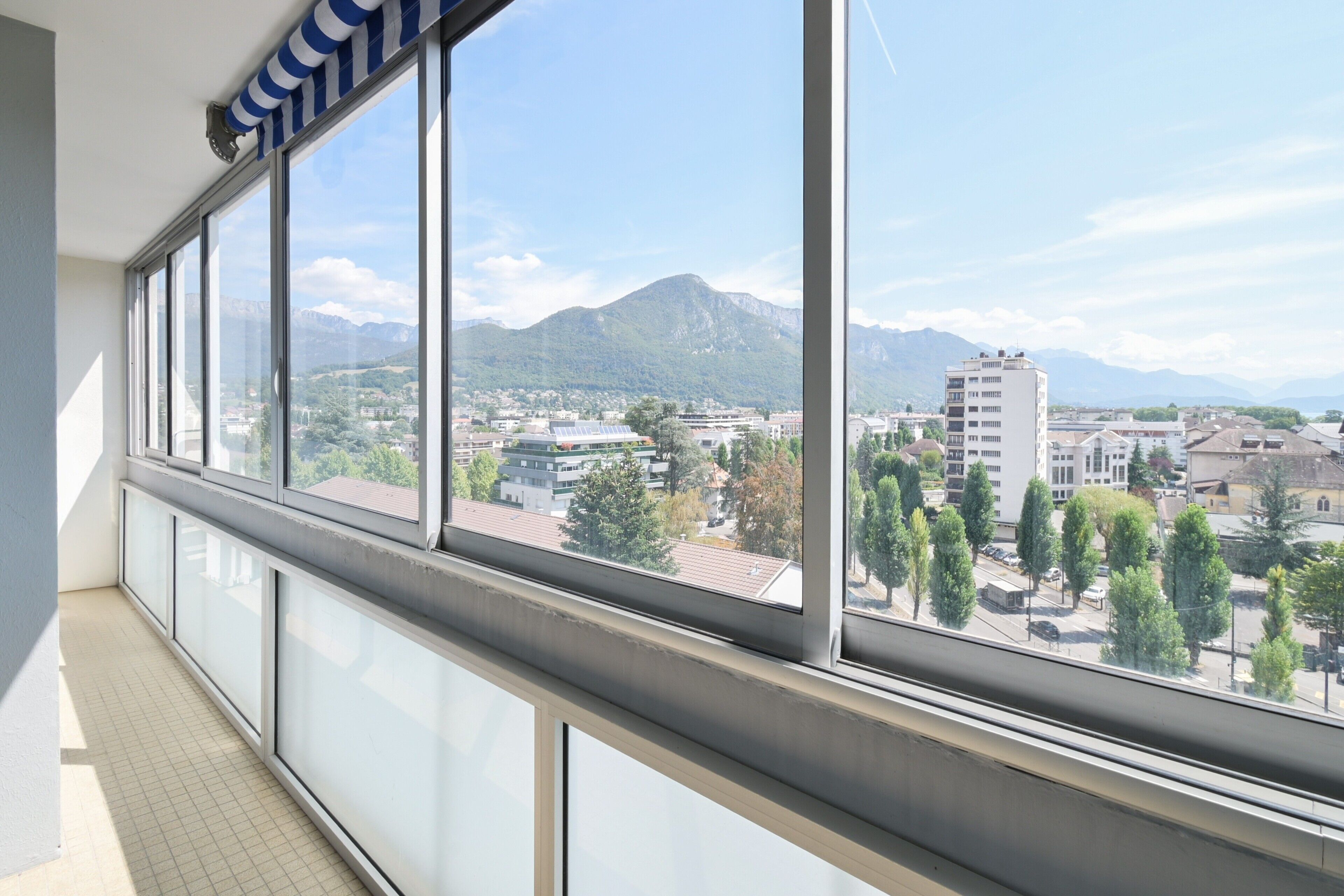 A balcony with large windows overlooking a cityscape with mountains in the distance.