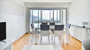 Ein modernes Wohnzimmer mit Essbereich, großen Fenstern und Blick auf Gebäude und Berge.