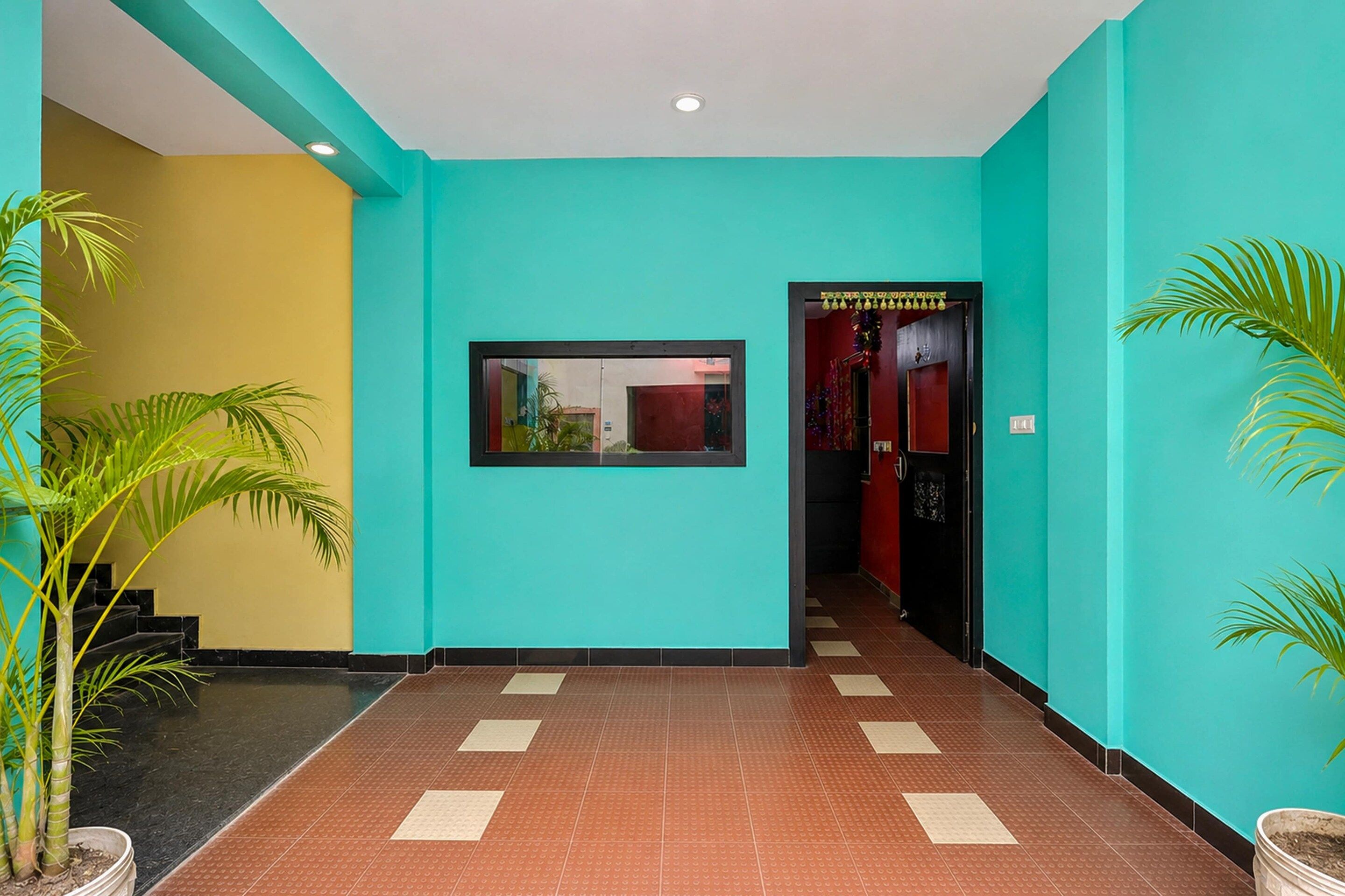 A hallway with a tiled floor, a framed picture on the wall, and potted plants.