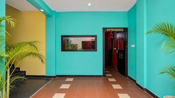 A hallway with a tiled floor, a framed picture on the wall, and potted plants.