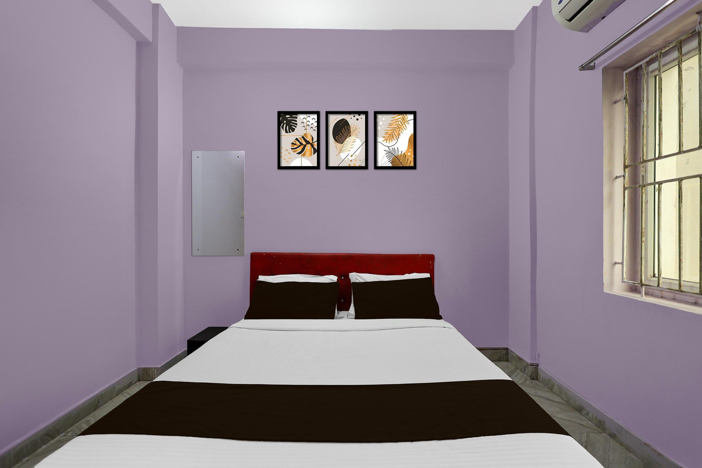 Una habitación con una cama, una ventana con barrotes y tres cuadros en la pared.