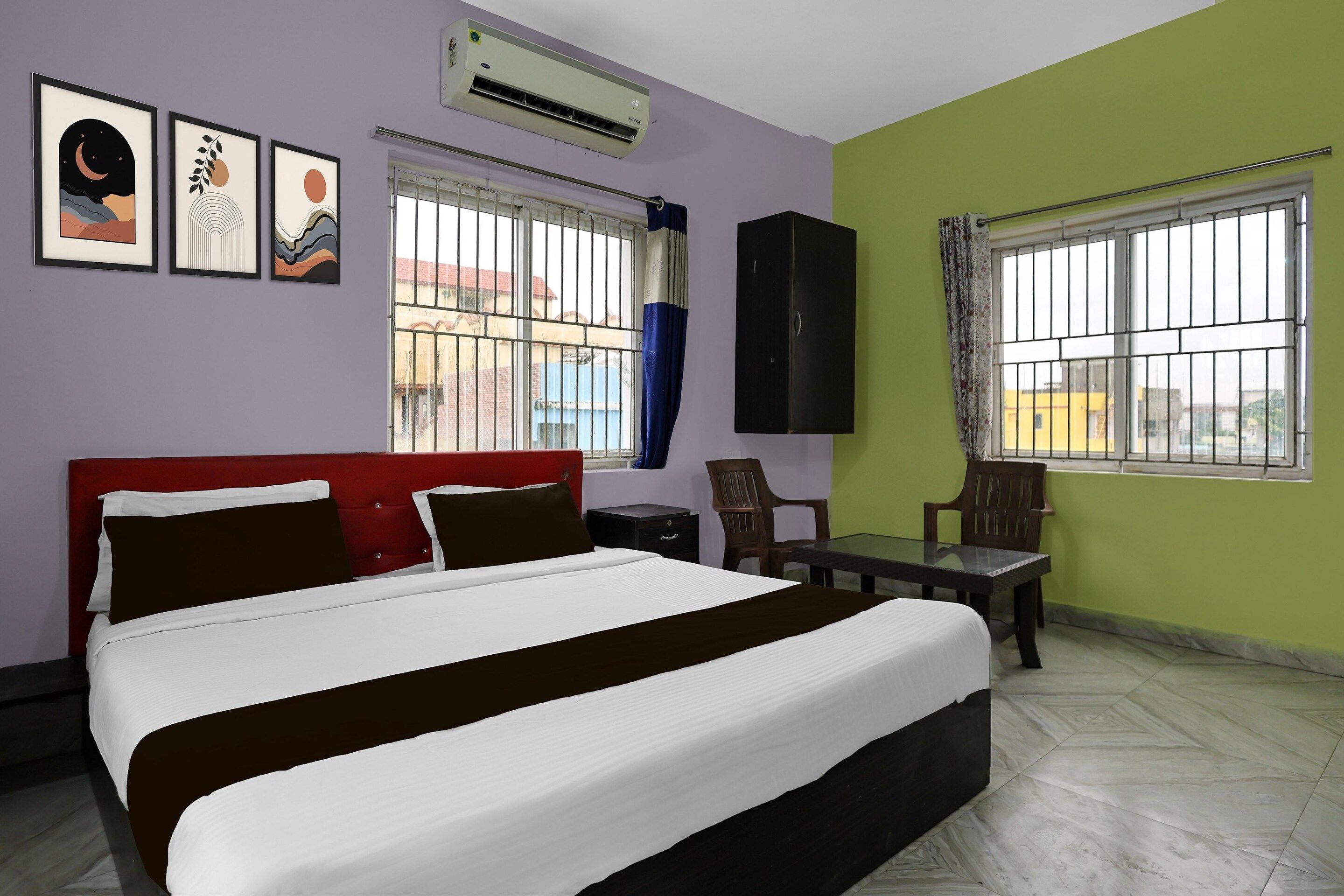 A hotel room with a bed, a desk, a chair, an air conditioner, and a window with bars.