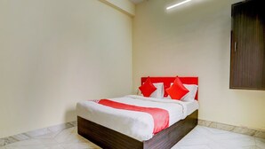 A neatly made bed with a wooden frame and red pillows, set on a patterned floor, in a room with plain walls and a ceiling light. - Classic Avisi Residency (Bhubaneshwar)