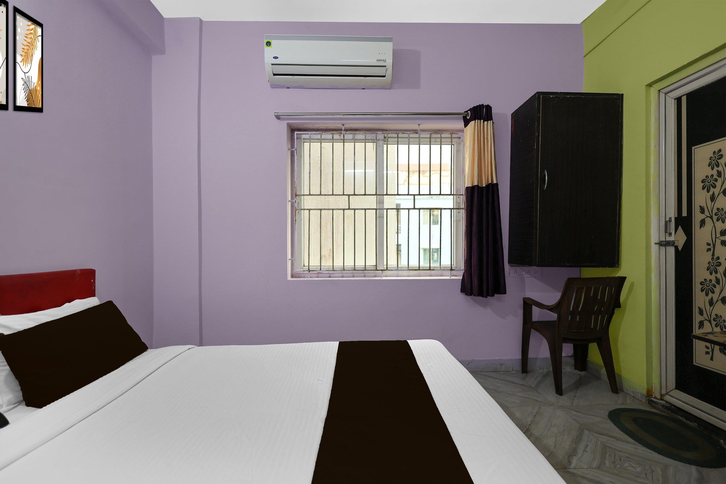 Un dormitorio con cama, ventana con rejas, aire acondicionado, armario y puerta con estampado floral.