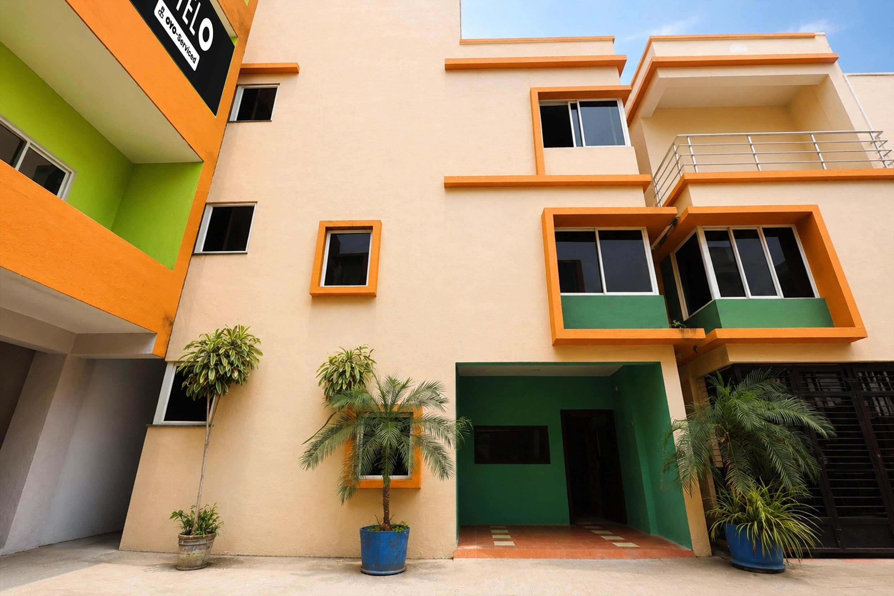 A modern building with multiple balconies, potted plants, and a green entrance.
