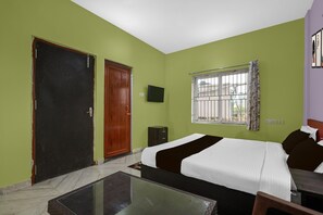 A hotel room with a bed, a small table, a window with bars, and a door. - Classic Avisi Residency (Bhubaneshwar)