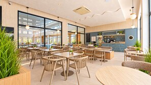 Una cafetería moderna con mesas dentro, una zona de bar y grandes ventanales.