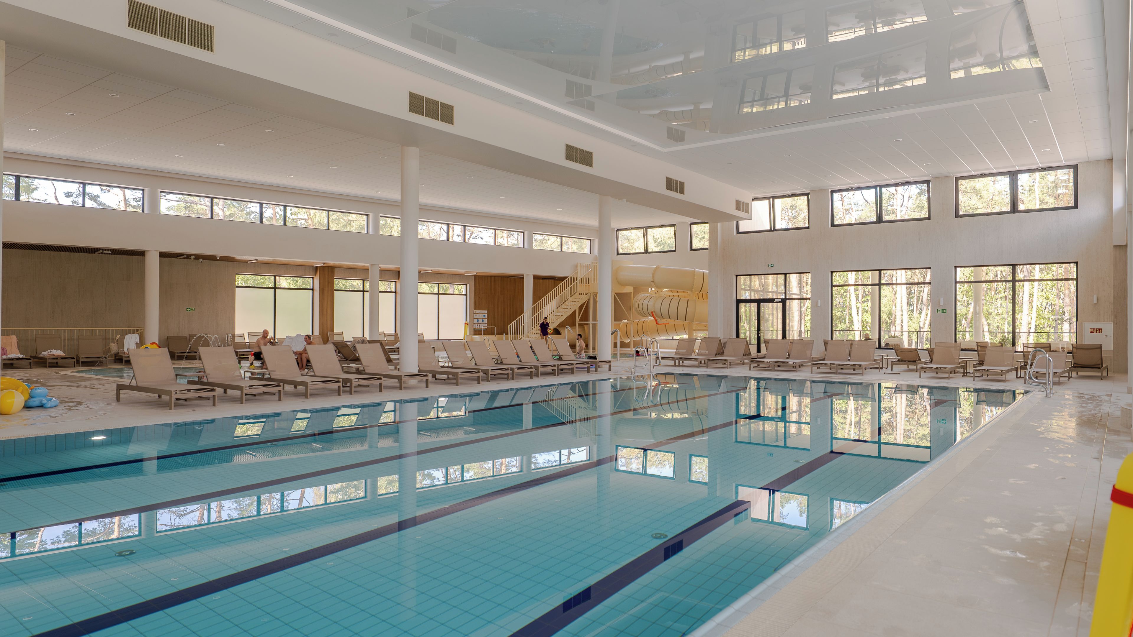 Una piscina interior con varias pistas, tumbonas y ventanas amplias.