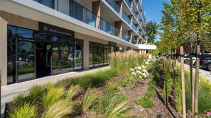 Un edificio moderno con escaparate que dice 'Strefa automatyw' y un jardín ajardinado con diversas plantas.