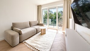 Una sala moderna con un sofá, una mesita redonda y vistas a un balcón con mobiliario exterior.