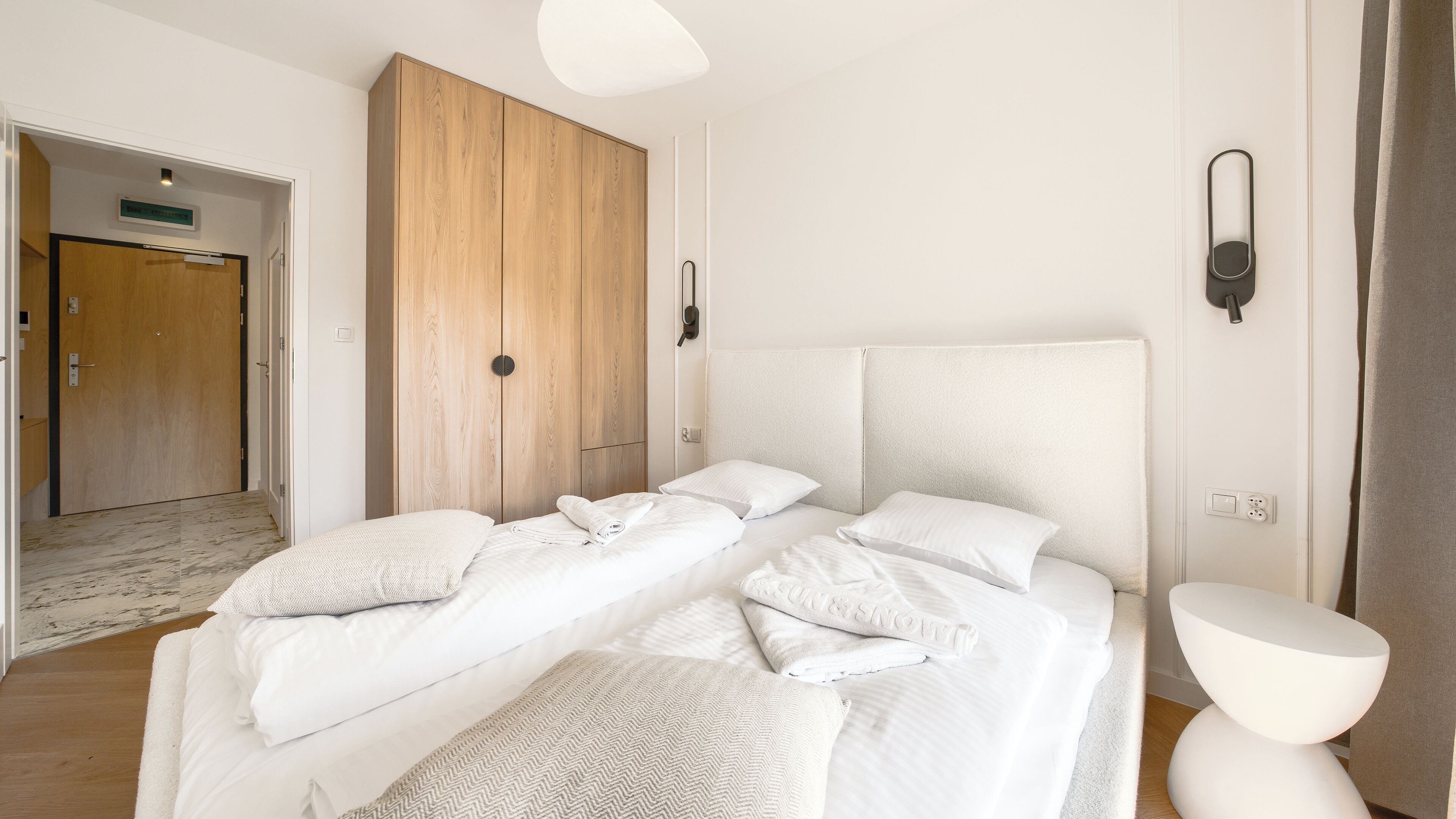 A hotel room with a large bed, two bedside tables, a wardrobe, and a door leading to another room.