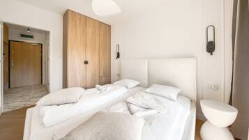 A hotel room with a large bed, two bedside tables, a wardrobe, and a door leading to another room.