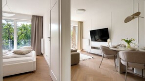 A modern living room with a sofa, a dining table with chairs, a flat-screen TV, and a view of greenery outside. - Apartamenty Sun & Snow Koniecznego (Dziwnów)