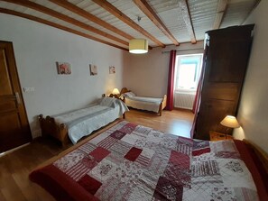 Ein Schlafzimmer mit zwei Einzelbetten, einer großen Steudecke, Holzbalken, einem Fenster mit Vorhängen und einem Heizkörper.