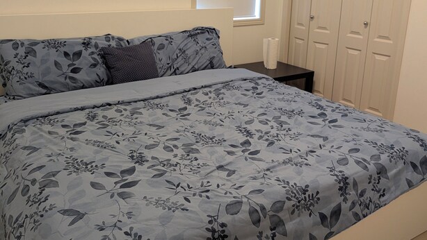Een slaapkamer met een bed, nachtkastje, raam en een kledingkast.