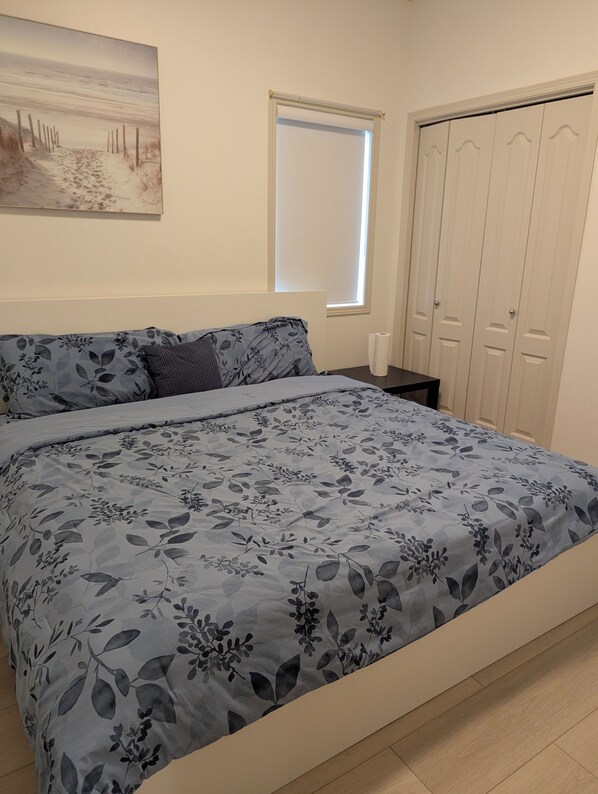 A bedroom with a bed, a nightstand, a window, and a wardrobe.