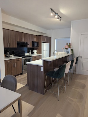 Una cocina moderna con armarios de madera oscura, electrodomésticos de acero inoxidable, una encimera blanca y una zona de bar con taburetes.