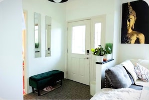 Una habitación con un banco verde, una puerta blanca, una planta en maceta y un cuadro de Buda.
