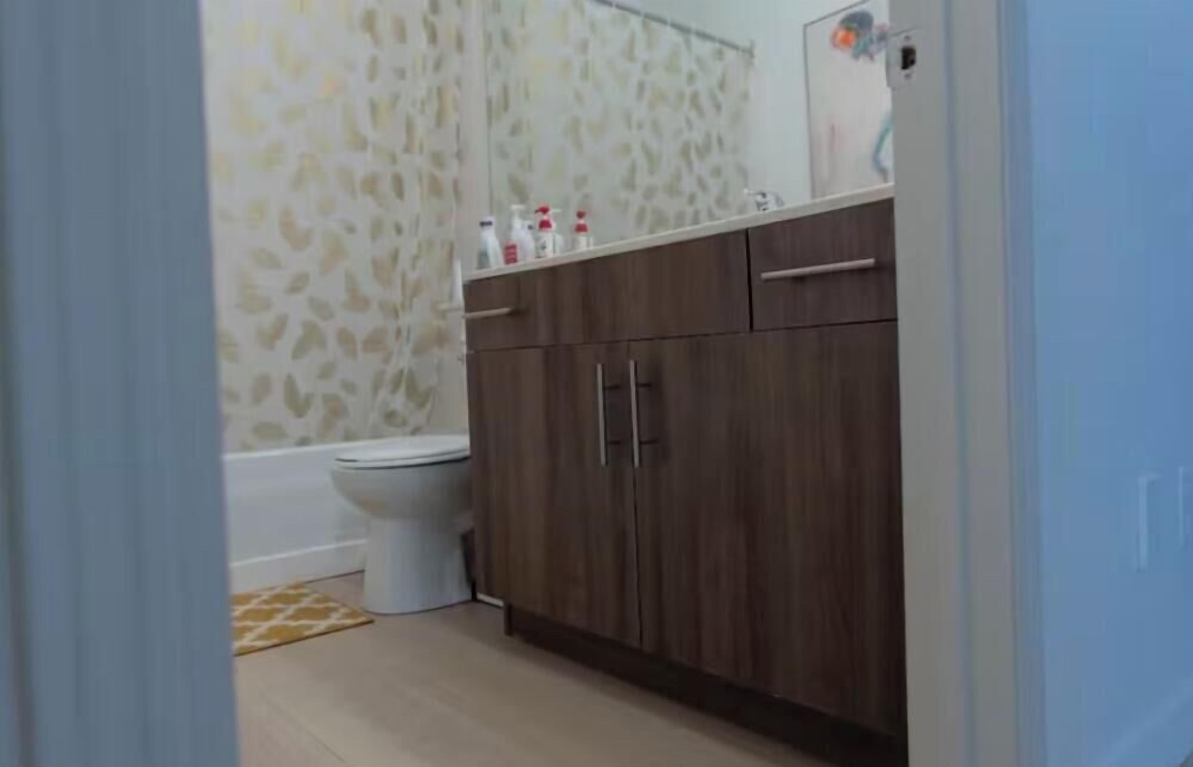 Ein Badezimmer mit Toilette, Holzschränken und einem duschvorhang mit Muster.