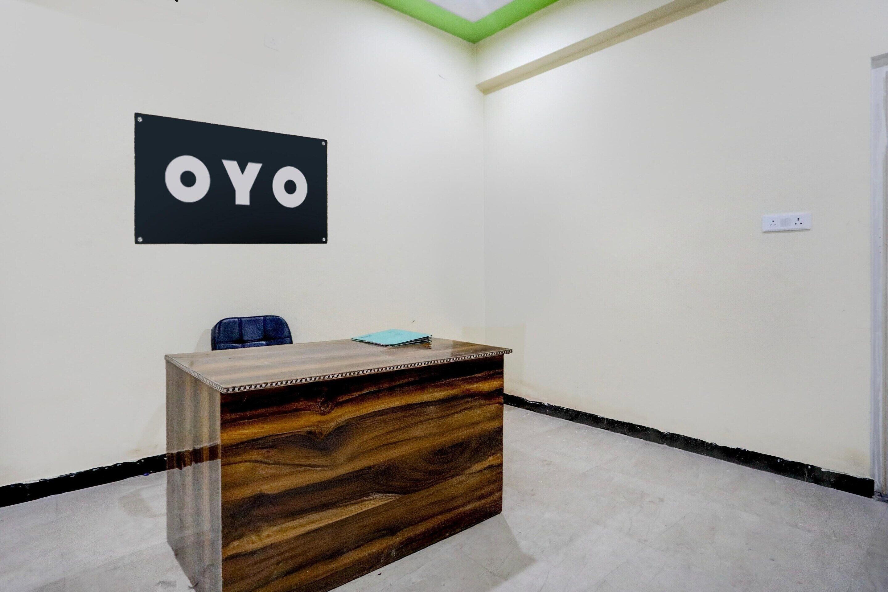 Eine Rezeption mit einem Schild, auf dem 'OYO' steht, in einem Raum mit weißen Wänden und einer grünen Decke.