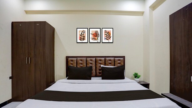 A hotel room with a large bed, a wooden wardrobe, and three framed artworks on the wall. - Classic SGD Lawn And Hotel (Varanasi)
