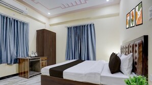 A hotel room with a bed, a wardrobe, a desk, and a potted plant. - Classic SGD Lawn And Hotel (Varanasi)