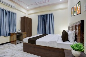 A hotel room with a bed, a wardrobe, a desk, and a potted plant. - Classic SGD Lawn And Hotel (Varanasi)