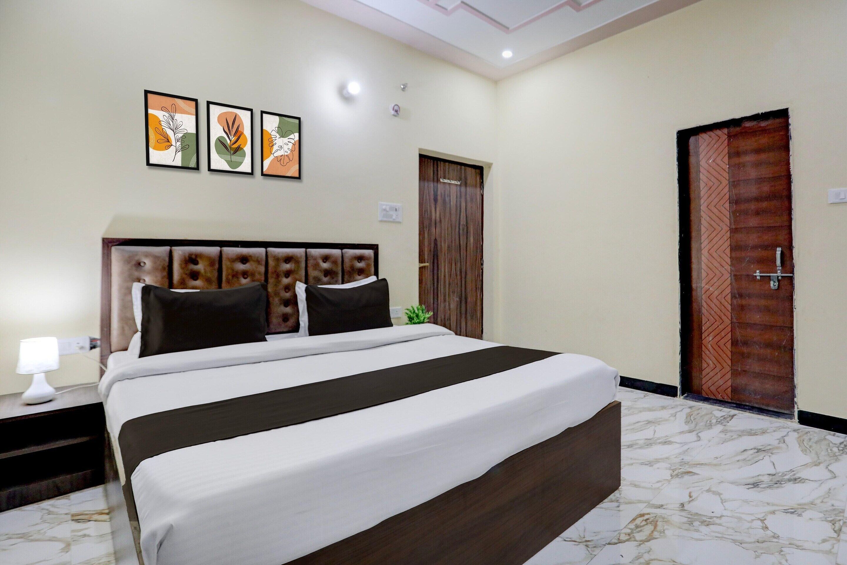 A hotel room with a bed, a nightstand, a lamp, a door, and three framed pictures on the wall.