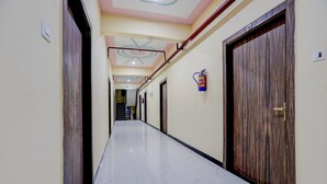 A hallway with a marble floor, wooden doors, and a fire extinguisher mounted on the wall. - Classic SGD Lawn And Hotel (Varanasi)