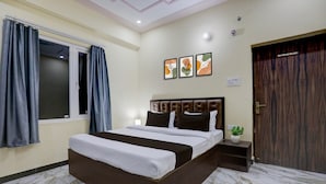 A hotel room with a bed, a nightstand, a potted plant, and a door. - Classic SGD Lawn And Hotel (Varanasi)