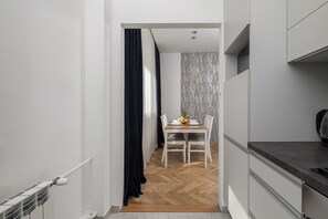 A narrow hallway leading to a dining area with a table set for two, a patterned wall, and a kitchen area with cabinets. - Lumina 3room Apart near Pałac Kultury (Warszawa)