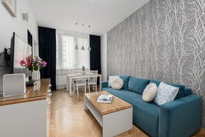 Un salon moderne avec un canapé bleu, une table basse et un coin repas comprenant une table et des chaises blanches.
