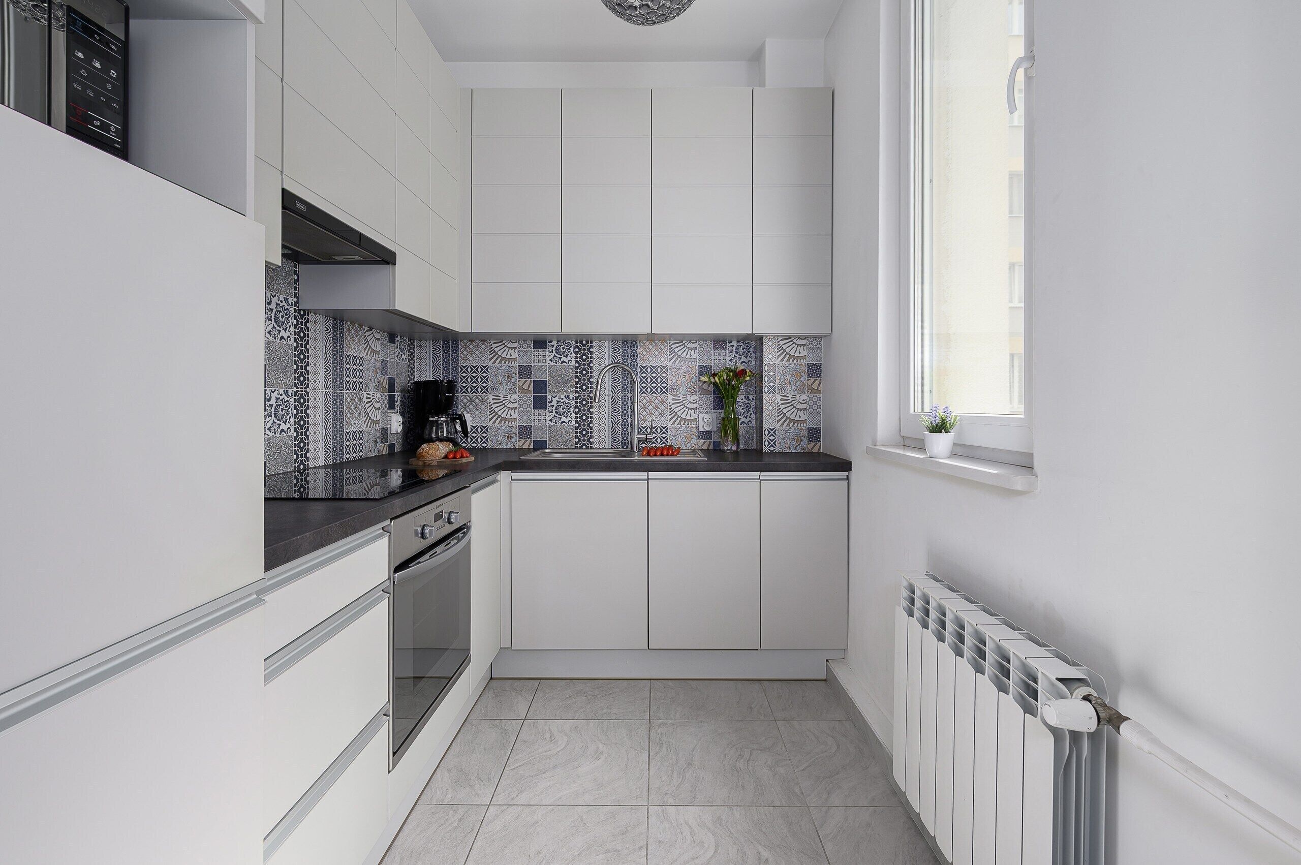 Eine moderne Küche mit weißen Schränken, einer strukturierten Rückwand und einem Fenster, das für natürliches Licht sorgt.