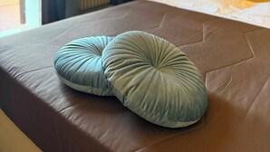 Un letto con una testiera marrone e due cuscini verdi, un comodino con una lampada e uno sfondo decorato con un motivo floreale.