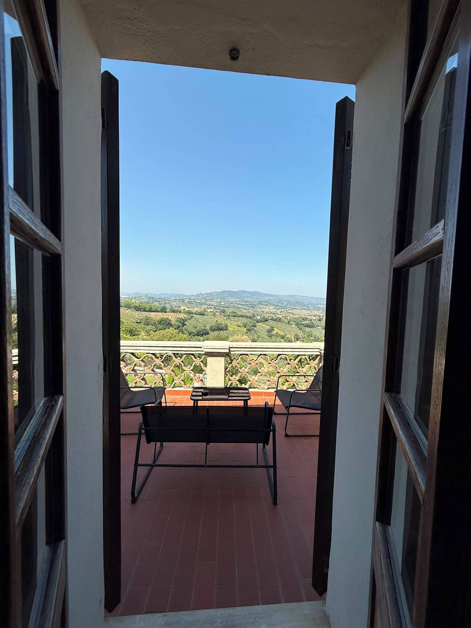 A balcony with a view of a hilly landscape, a table, and two chairs.