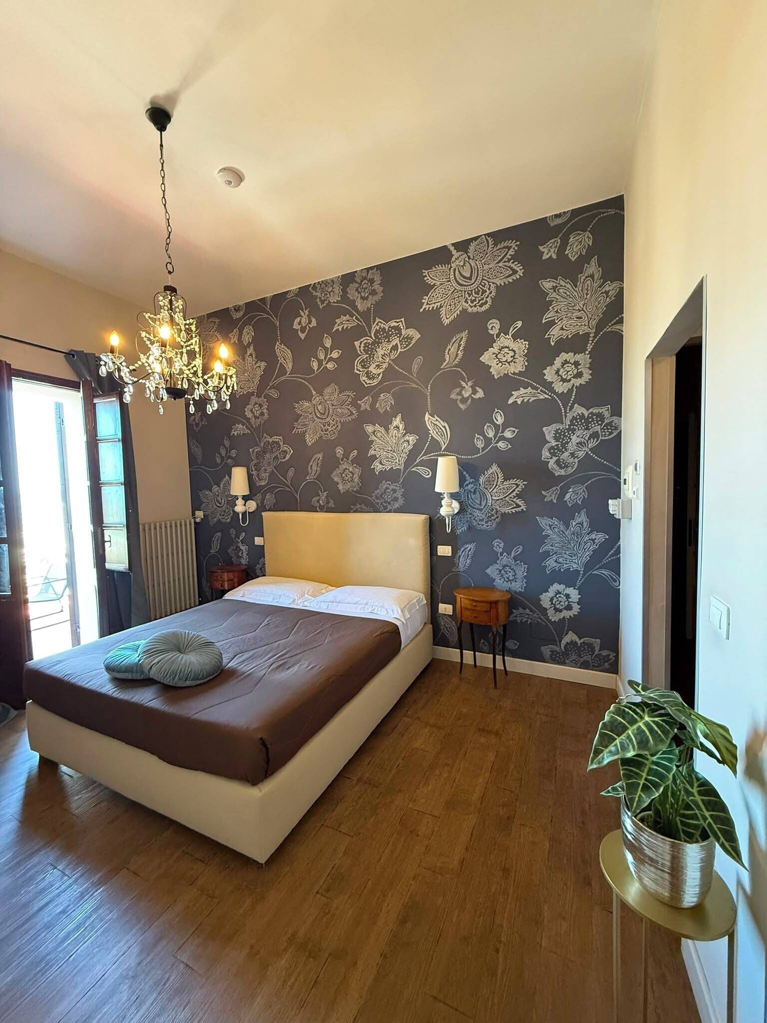 Un dormitorio con una cama grande, una araña, una planta en maceta y un papel tapiz floral.