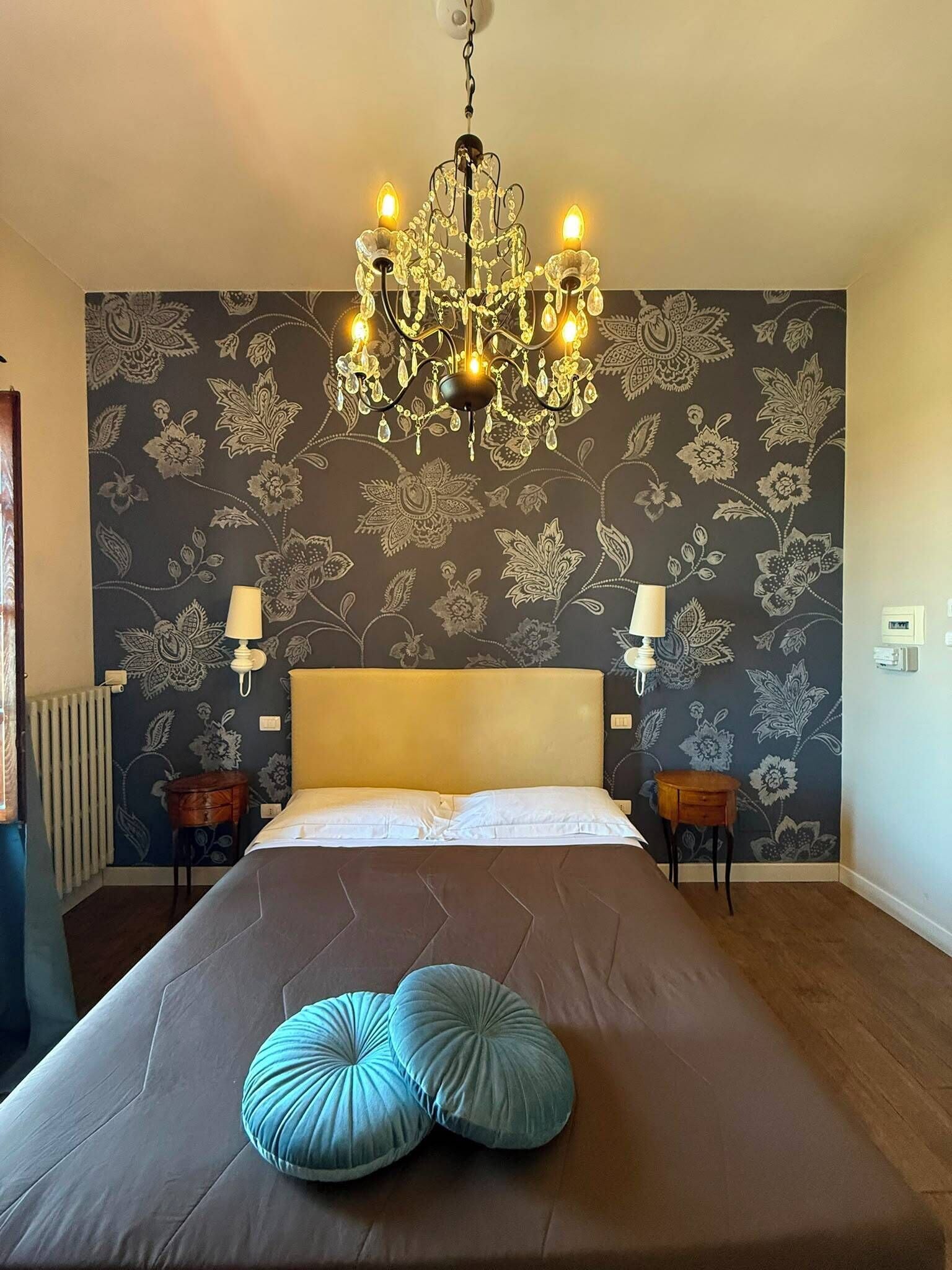 A bedroom with a large bed, a chandelier, two bedside lamps, and floral wallpaper.