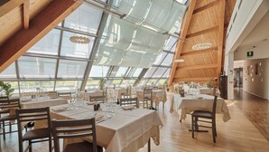 Un comedor amplio con techos altos y ventanas grandes, que presenta vigas de madera y una lámpara moderna.
