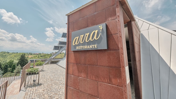 En skilt med restaurantens navn 'AURA RISTORANTE' monteret på en murstensvæg.