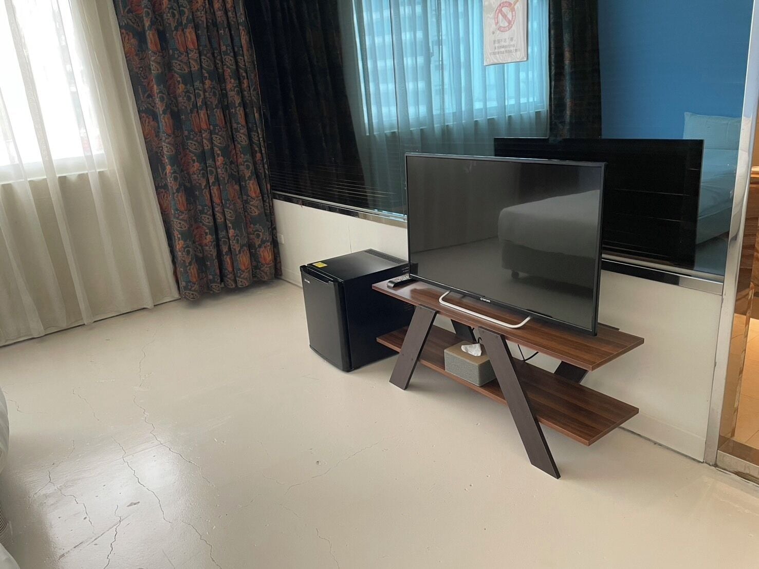 Una sala moderna con un televisor de pantalla plana sobre un soporte de madera, un altavoz negro pequeño y una ventana con cortinas.