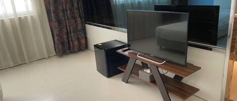 Una sala moderna con un televisor de pantalla plana sobre un soporte de madera, un altavoz negro pequeño y una ventana con cortinas.
