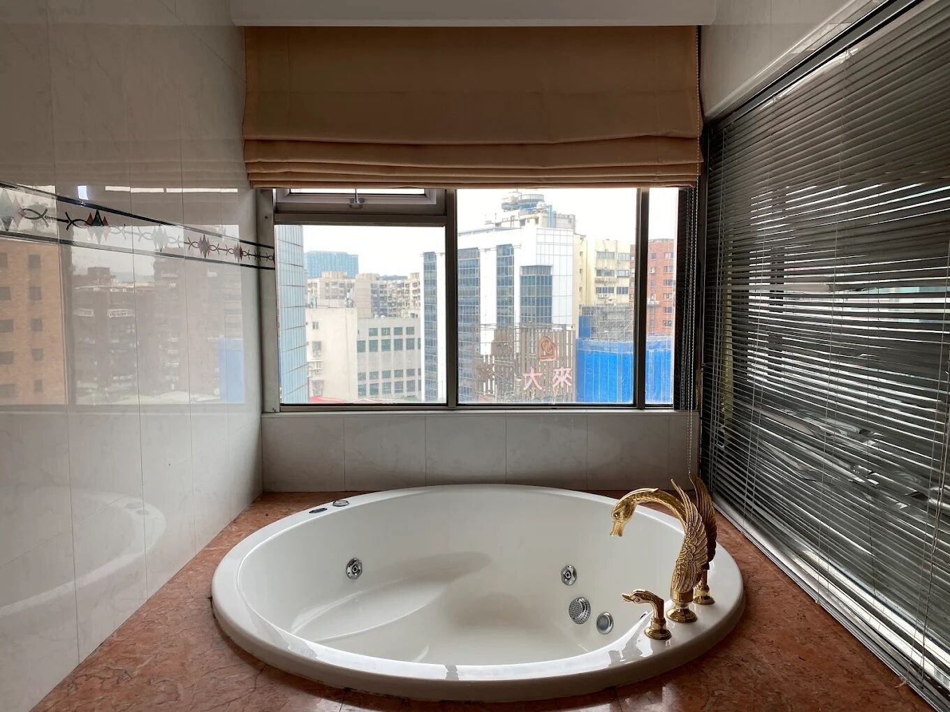 Un baño moderno con una bañera independiente, un ventanal con vistas a edificios de la ciudad y un espejo grande.