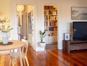 A living room with a wooden floor, a dining table with chairs, a bookshelf, a television, and a potted plant. - Cute & cosy family home - close to the city (Brompton)
