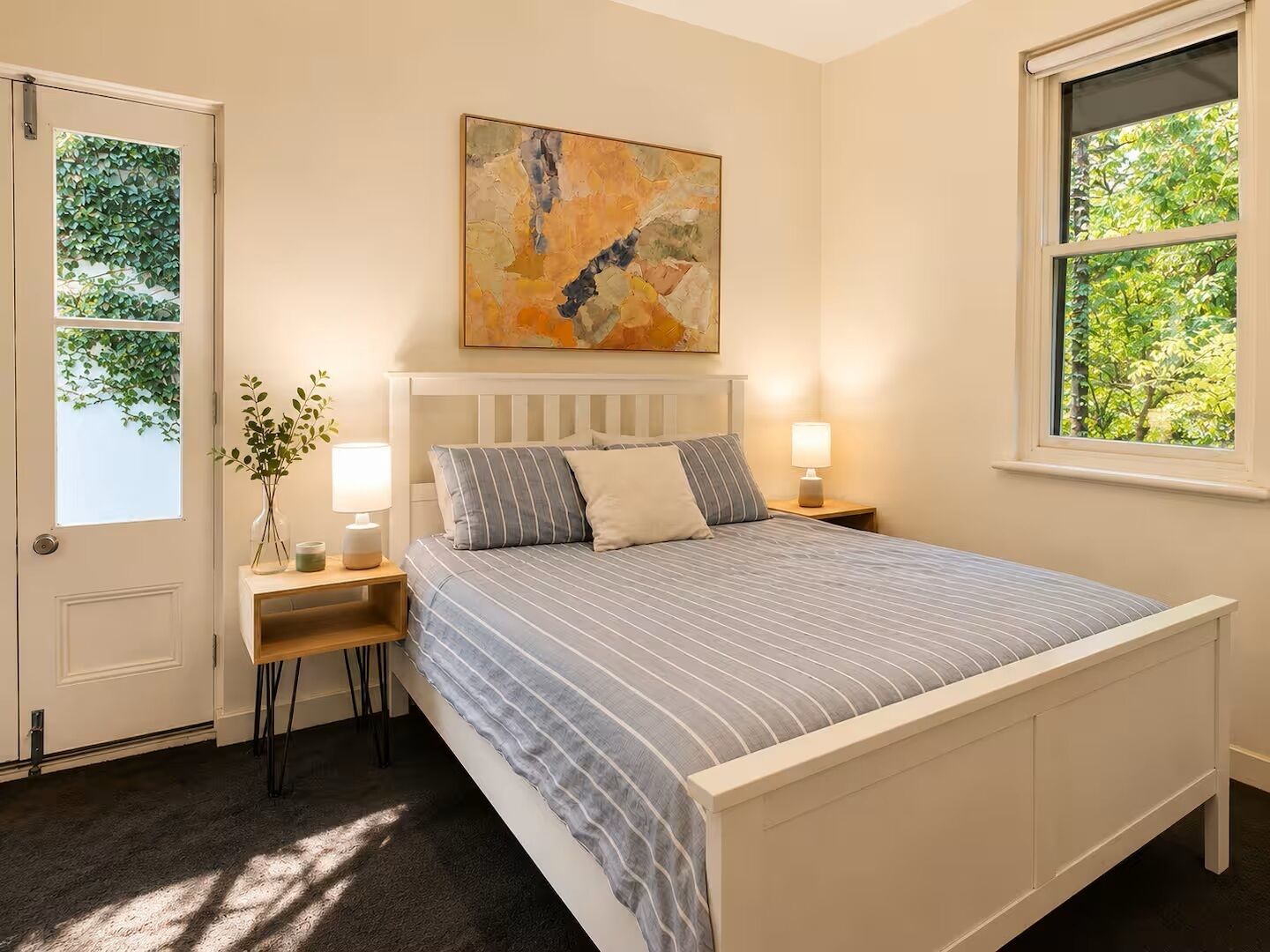 A bedroom with a bed, bedside tables, a window, and a painting on the wall.