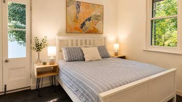 A bedroom with a bed, bedside tables, a window, and a painting on the wall.