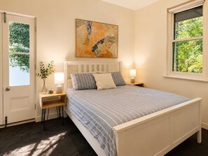 A bedroom with a bed, bedside tables, a window, and a painting on the wall. - Cute & cosy family home - close to the city (Brompton)