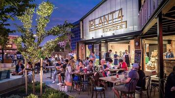 An outdoor seating area with tables and chairs, a building with a sign reading 'PLANTA BOWDEN,' and a person standing at a counter.