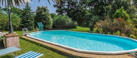 A swimming pool with a wooden deck, surrounded by grass and trees.