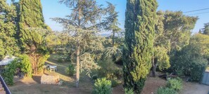 Un jardin avec de grands arbres, un mur de pierre et une table et une chaise blanches.